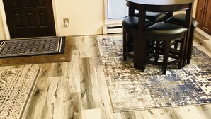 A room with a wooden floor, a round table with chairs, a door, and a wall-mounted light fixture. - Home away from Home!!  (Boise)