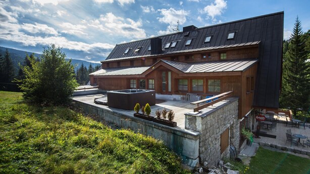 Un edificio moderno de varios pisos con un amplio patio exterior, un jacuzzi y un muro de contención de piedra.