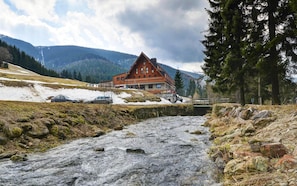 Et lodge med rød facade, en flod foran og bjerge i baggrunden.