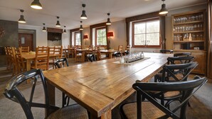Un comedor espacioso con varias mesas y sillas de madera, iluminación colgante y una vinoteca con copas.