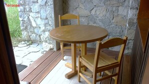 A wooden table and chairs in a stone-walled room with a view of greenery outside. - Valmorel apartment (4 people 30 m2) back to the skis .Terrace with porch. (Les Avanchers-Valmorel)