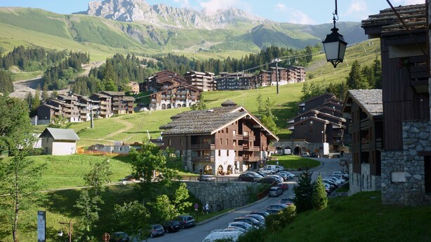 A mountain resort with multiple chalet-style buildings, a parking lot, and a view of the surrounding mountains. - Valmorel apartment (4 people 30 m2) back to the skis .Terrace with porch. (Les Avanchers-Valmorel)