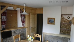 A wooden dining table with chairs, a vase with flowers, and a stone wall. - Valmorel apartment (4 people 30 m2) back to the skis .Terrace with porch. (Les Avanchers-Valmorel)