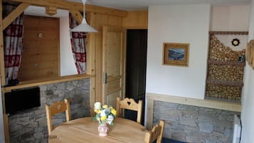 Une table à manger en bois, des chaises, un vase rempli de fleurs et un mur en pierre.