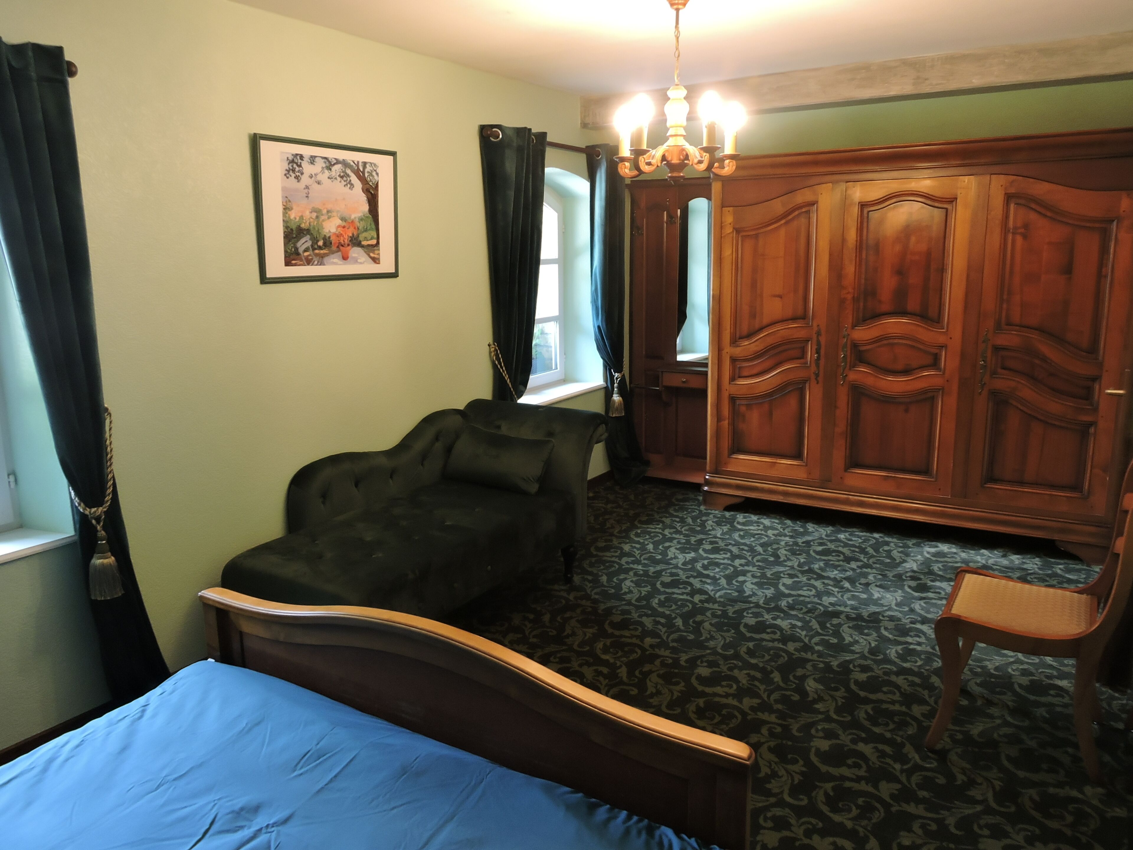 Ein Schlafzimmer mit Bett, Kleiderschrank, Stuhl, Schreibtisch und einem Fenster mit Vorhängen.