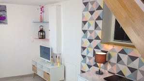 A modern, minimalist room with a white desk, a laptop, and a lamp. There is a shelf with decorative items and a framed picture on the wall. - Triplex, Beautiful apartment of 50 sqm on 3 levels, up to 4 people (Caen)