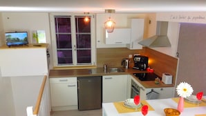 A compact kitchen with a dishwasher, a coffee maker, and a toaster. There is a dining table set with plates, a vase with a flower, and a bowl of fruit. - Triplex, Beautiful apartment of 50 sqm on 3 levels, up to 4 people (Caen)
