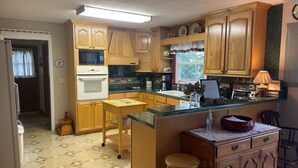 A kitchen with wooden cabinets, a microwave, an oven, a sink, and a dining area with stools.