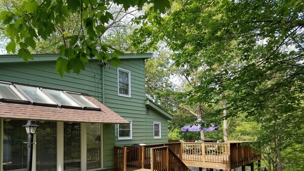 A green house with a covered porch, a wooden deck, and a small outdoor seating area.
