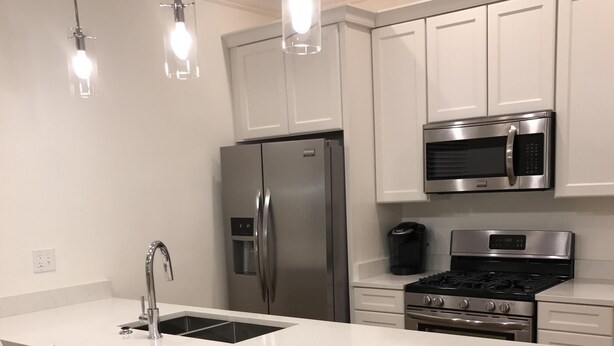 A modern kitchen with a central island, stainless steel appliances, white cabinetry, and pendant lighting.