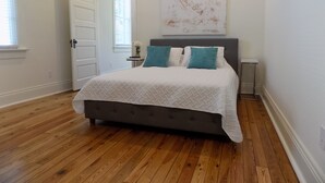 A bedroom with a bed, a door, a window, and a painting on the wall.