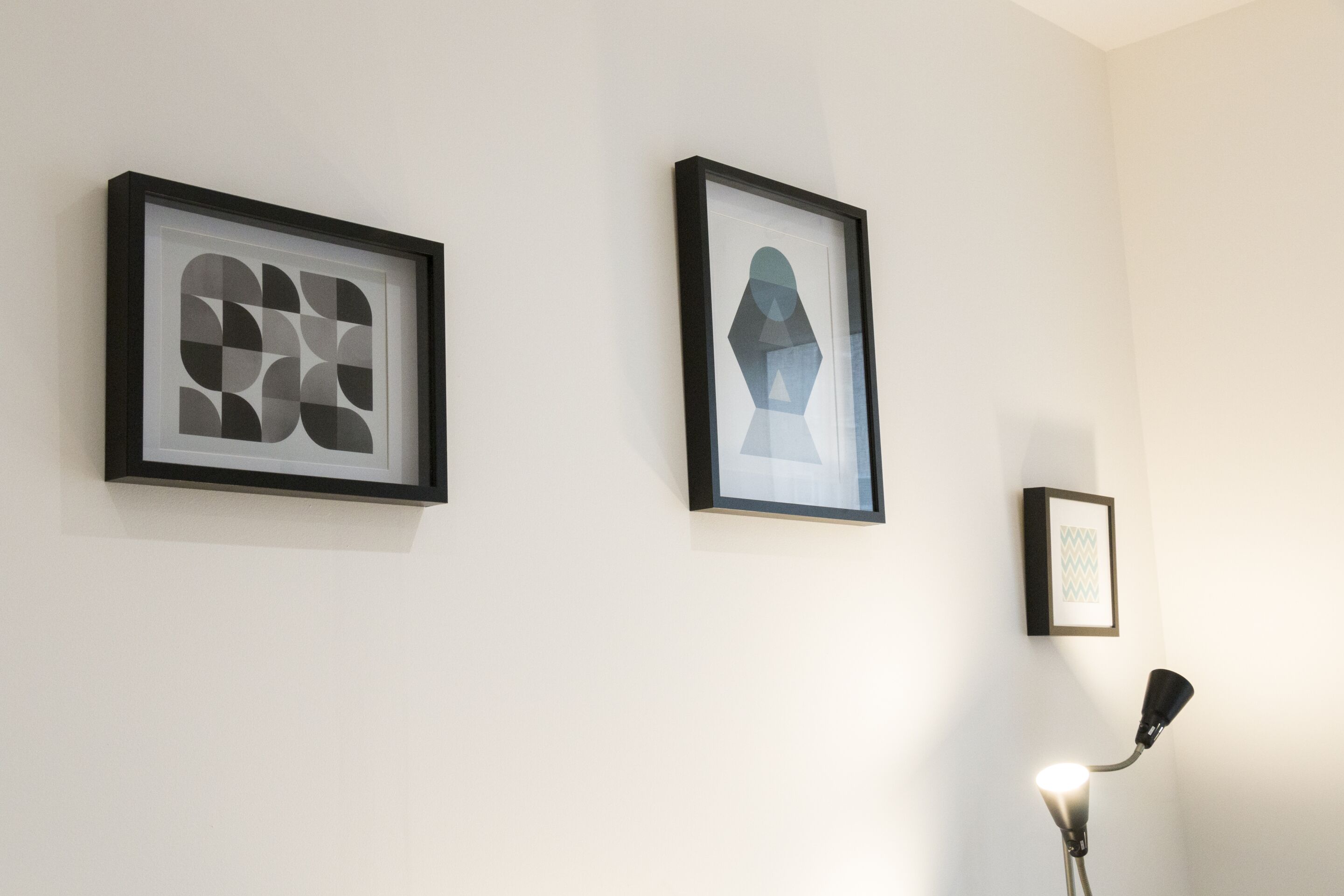 Deux œuvres d’art encadrées sont accrochées au mur, ainsi qu’une lampe et une photographie encadrée, dont on ne voit qu’une partie.