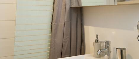 Un baño con lavamanos blanco, un espejo, cortina de ducha y una planta en maceta.