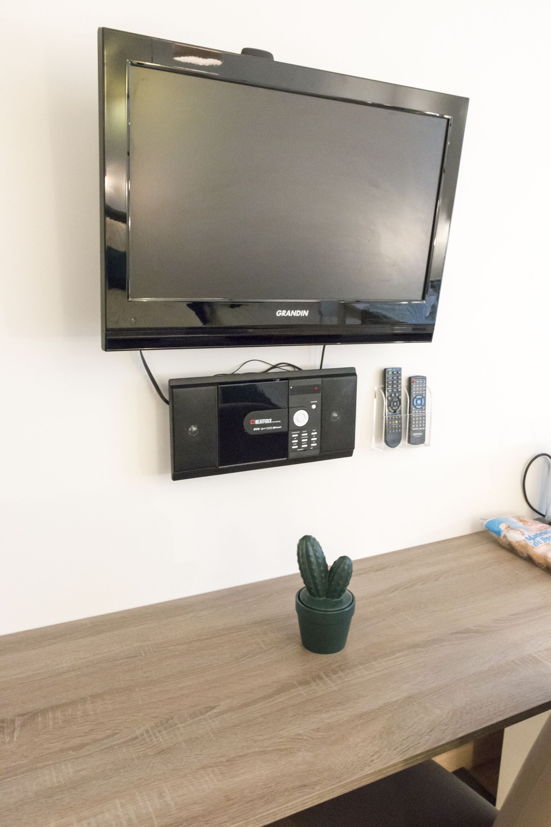 A flat-screen television mounted on a wall with a remote control and a media player below it.