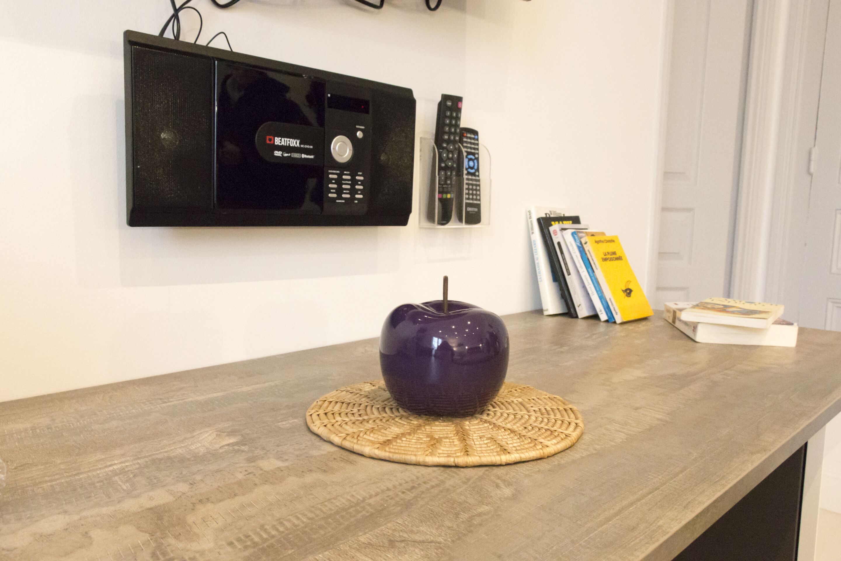 Een houten receptiebalie met een geweven onderzetter, een decoratieve vaas en een radio met afstandsbedieningen ernaast.