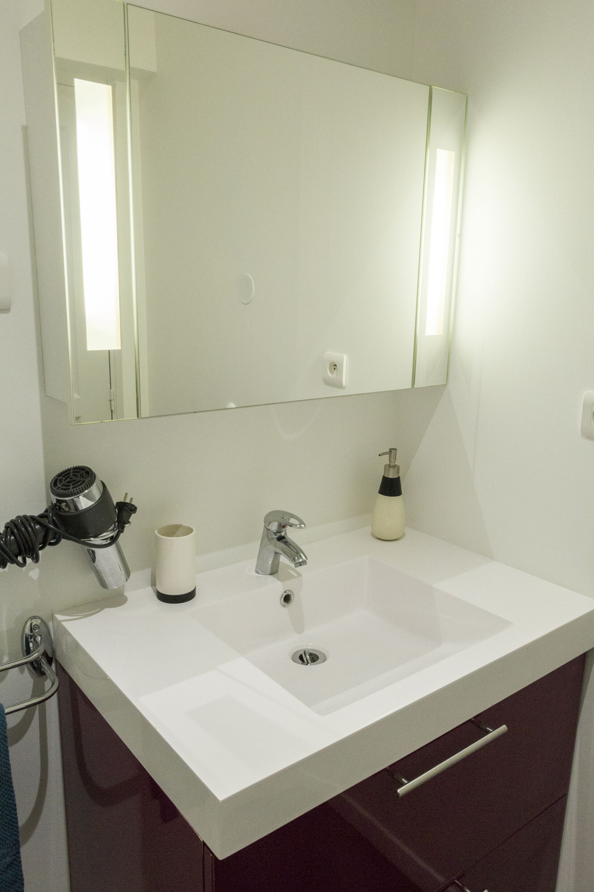 A bathroom with a white sink, a mirror, a towel rack, and a bottle of hand soap.