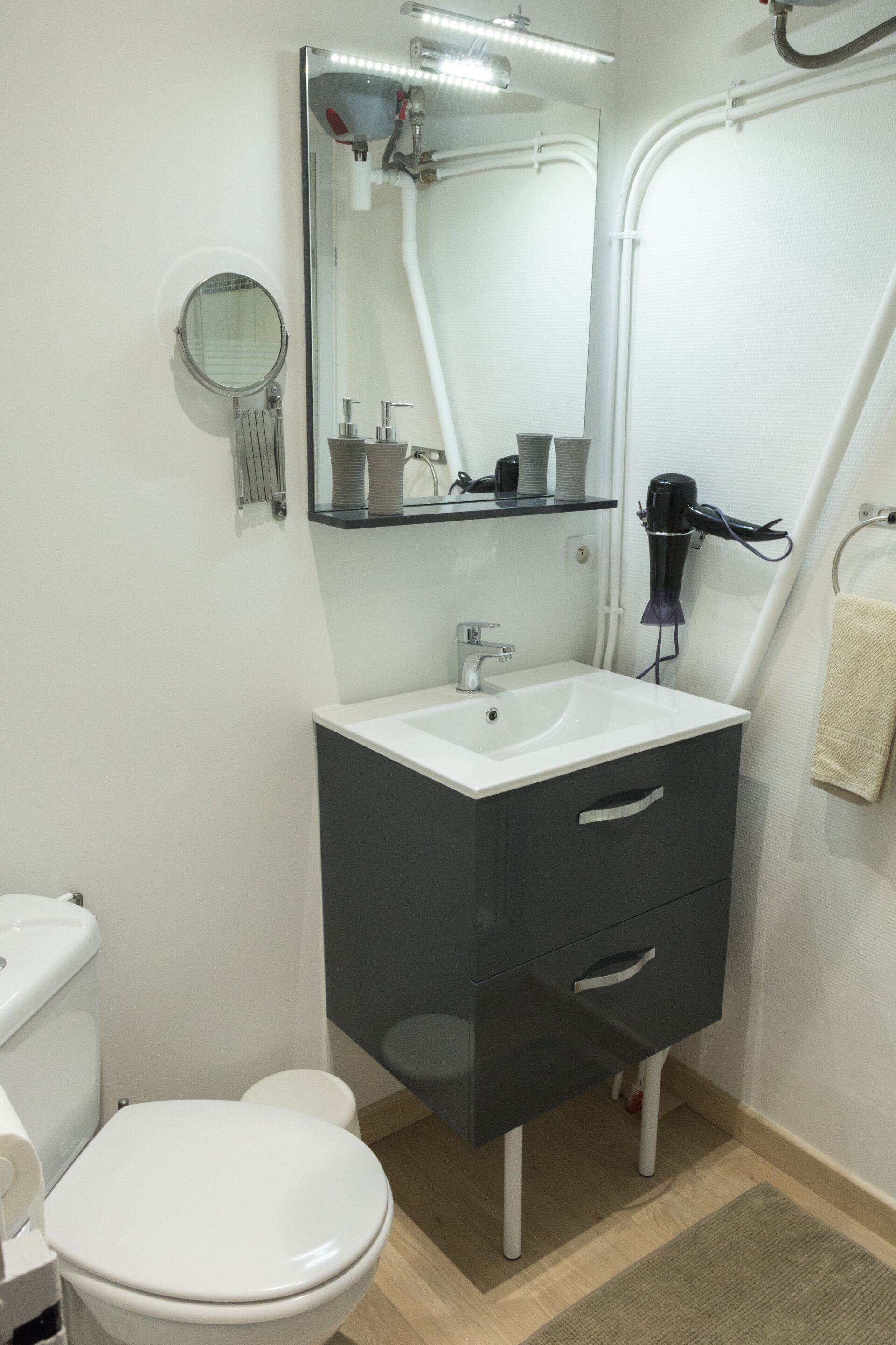 Une salle de bain avec des toilettes blanches, un lavabo avec un miroir au-dessus et un porte-serviettes.