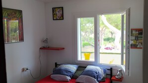 Ein Schlafzimmer mit Bett, Fenster, rotem Regal und Wandlampe.