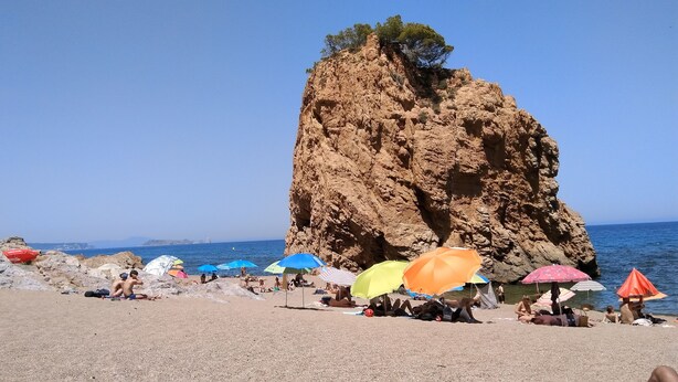 Ein felsiger Strand mit badenden Personen und bunten Sonnenschirmen.