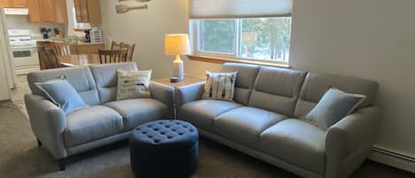 A living room with a sectional sofa, ottoman, and a dining area with a table and chairs.