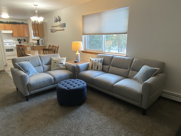 A living room with a sectional sofa, ottoman, and a dining area with a table and chairs.