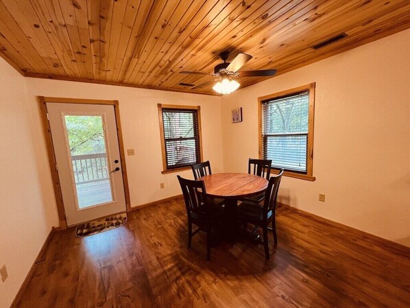 A dining area with a wooden table and chairs, a ceiling fan, and windows with blinds.