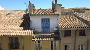 A building with a tiled roof, a balcony with a metal railing, and a window with shutters. - conditioning housing and equipped view roofs central, separate bedroom (Aix-en-Provence)