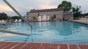 Una piscina con solárium de ladrillo, sillas de descanso y un edificio al fondo.
