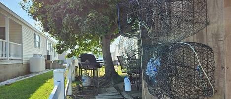 Un patio trasero cercado con una parrilla, mobiliario exterior y un árbol, delimitado por una valla de madera.