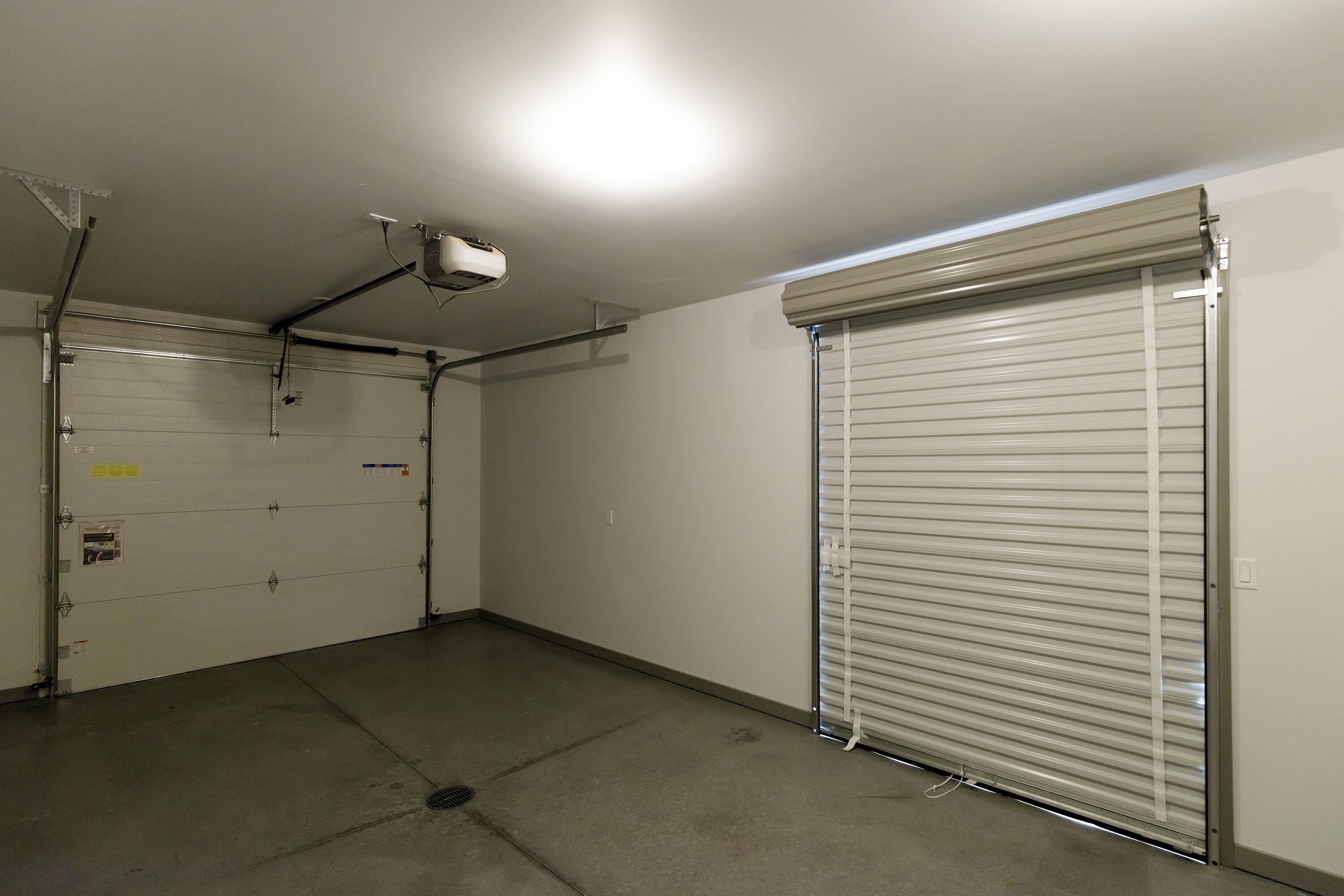 A clean, empty garage with a closed roller door and a ceiling-mounted projector.