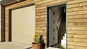 Un bâtiment moderne avec une façade en bois, une porte de garage et un pot de fleurs à l’extérieur.