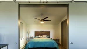 Une chambre à coucher avec un lit, un ventilateur de plafond, une table de chevet et une lampe.