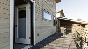 Un immeuble résidentiel doté d’une porte-fenêtre coulissante, d’un petit espace patio avec une table et des chaises, et d’une clôture en bois.