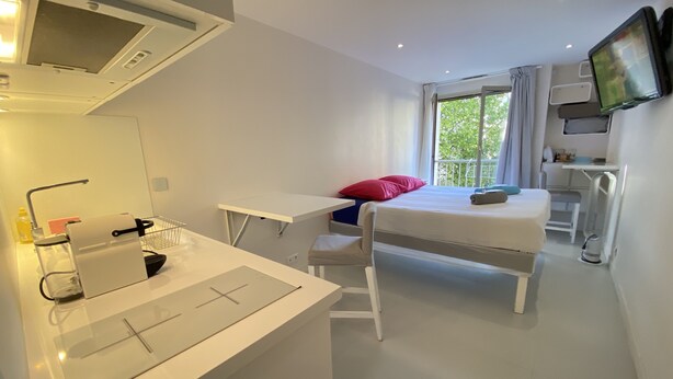 Ein modernes Hotelzimmer mit einem weißen Bett, einem Schreibtisch, einem Spiegel und einem Fernseher.