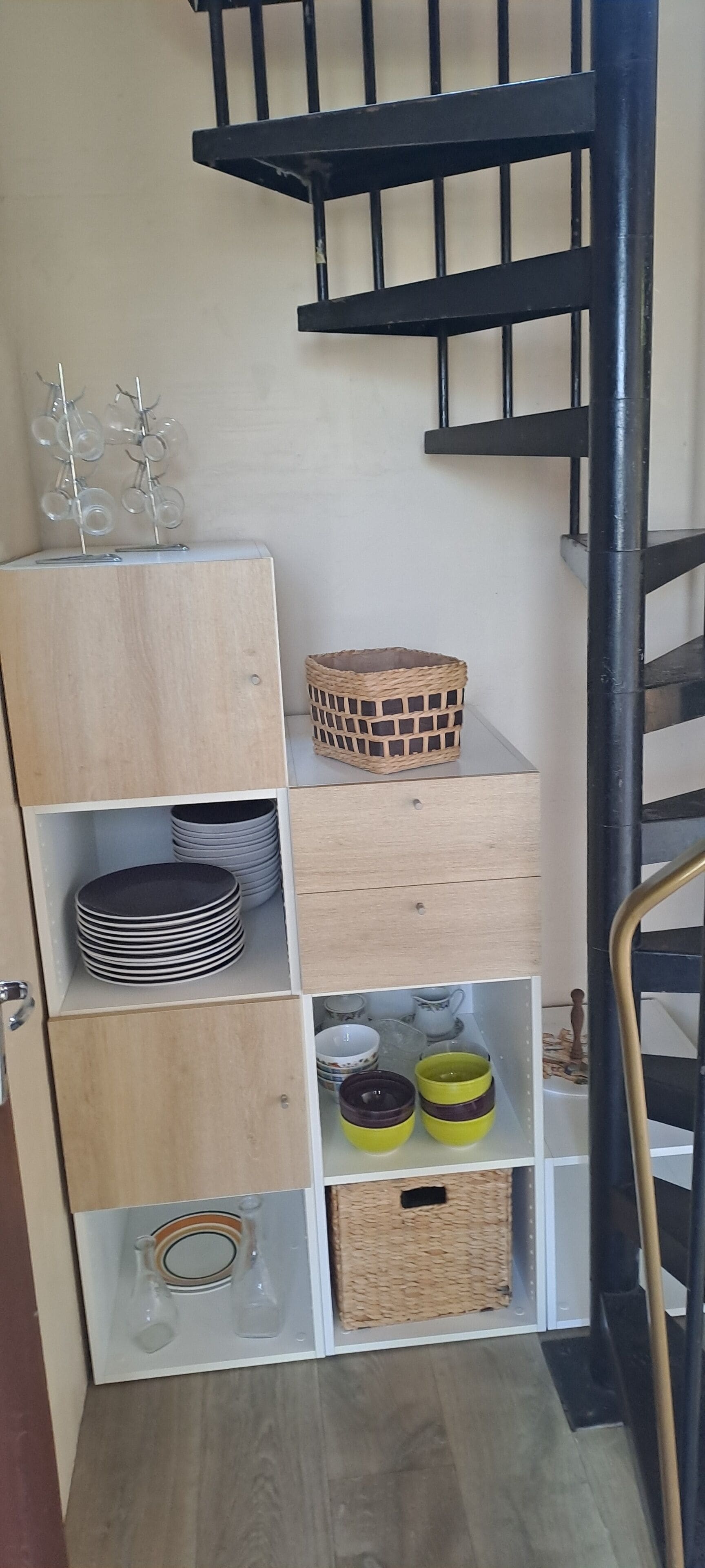 A wooden storage unit with shelves holding plates, bowls, and baskets.