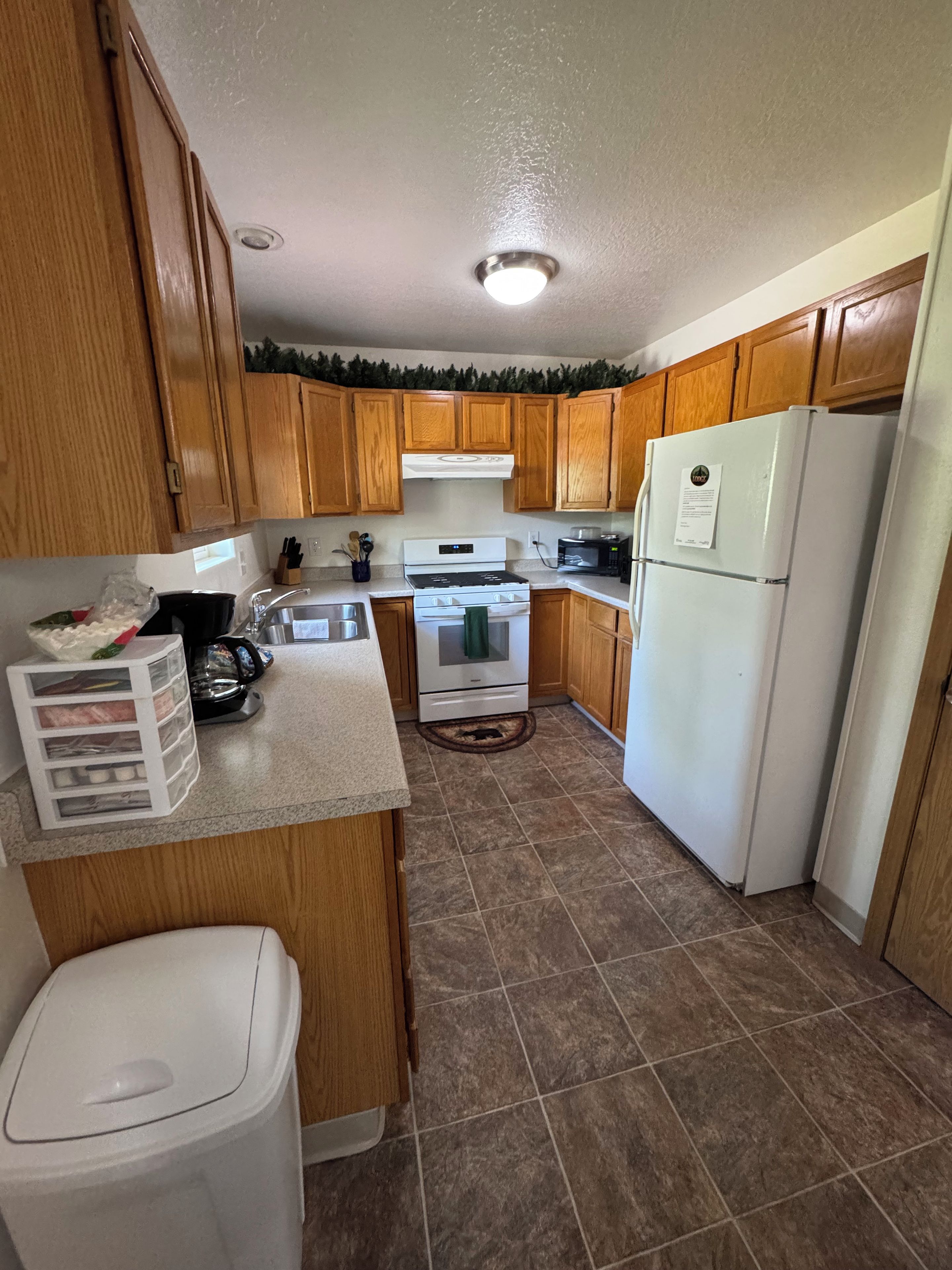 A kitchen with wooden cabinets, a white stove, a refrigerator, and a trash can.
