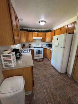 A kitchen with wooden cabinets, a white stove, a refrigerator, and a trash can.