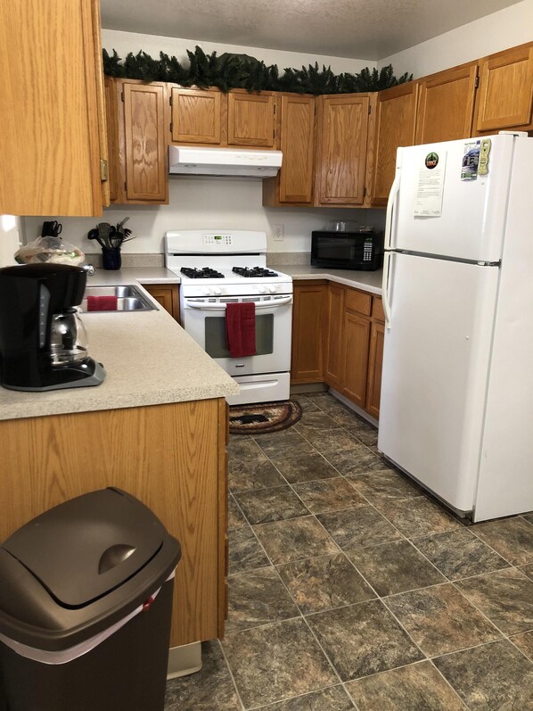 A kitchen with wooden cabinets, a white stove, a microwave, and a refrigerator. - 2 bedroom, 1 bath quiet lodge close to town with forest views!  (Soldotna)
