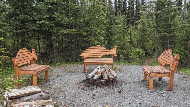 Un campeggio con tre poltrone in legno di stile Adirondack disposte attorno a un braciere con tronchi di legna.