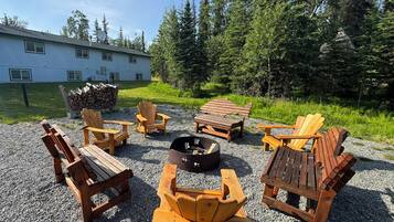 An outdoor seating area with Adirondack chairs and a fire pit, surrounded by gravel and trees.