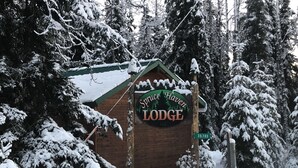 Una baita di legno con un cartello che recita "Spring Haven Lodge LLC", circondata da alberi coperti di neve.