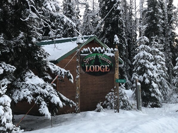A wooden lodge with a sign reading "Spring Haven Lodge LLC" surrounded by snow-covered trees. - 2 bedroom, 1 bath quiet lodge close to town with forest views!  (Soldotna)