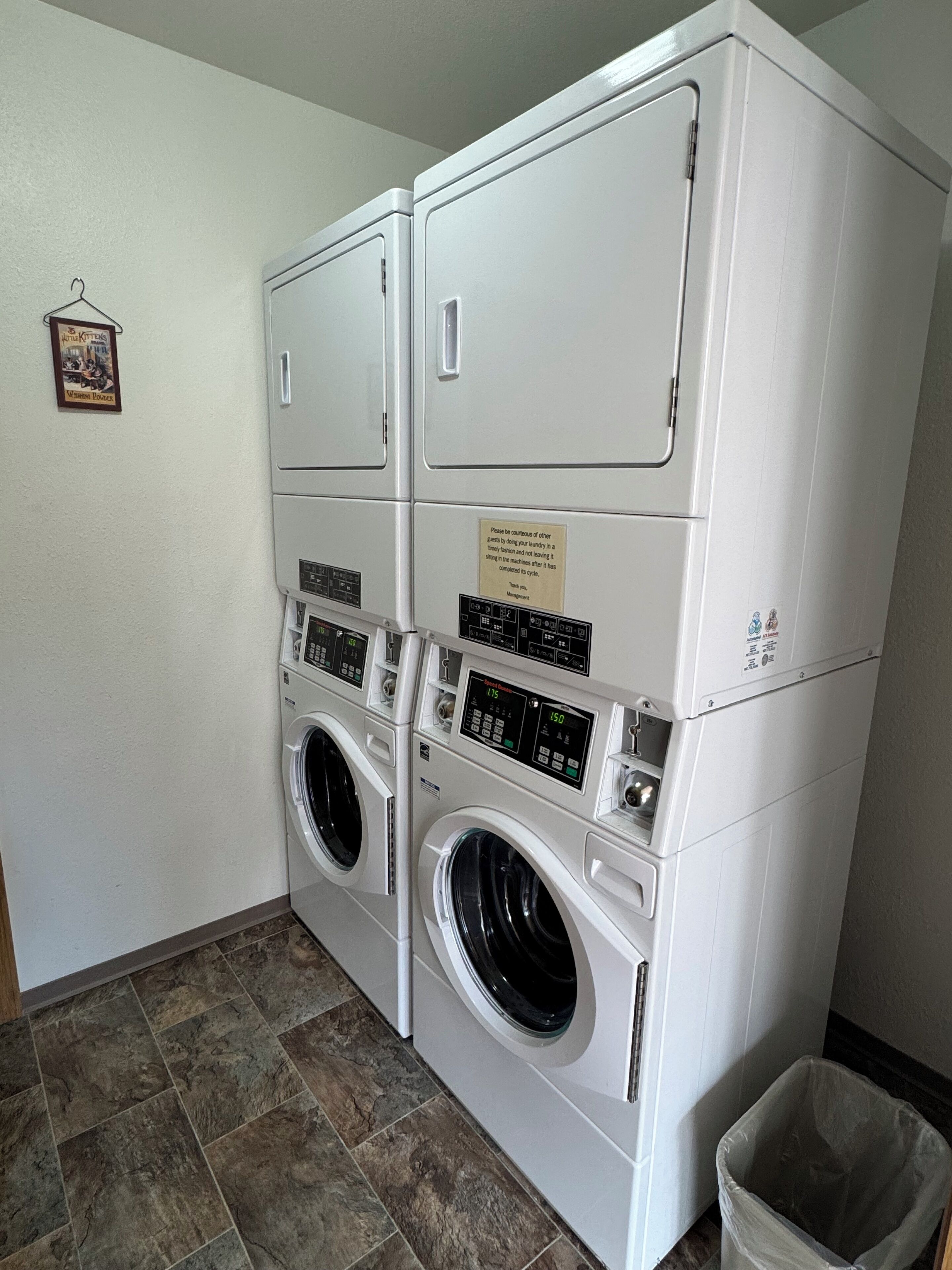 Una sala de bugaderia amb dues rentadores frontals apilades i una màquina d'assecar roba penjada a la paret.