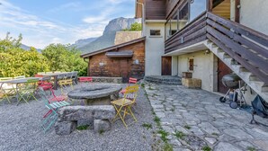 Une terrasse extérieure moderne, dotée d’un sol en pierre, d’un barbecue et de chaises colorées.
