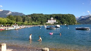 Une scène au bord du lac avec des bateaux, des nageurs et un bâtiment en arrière-plan.
