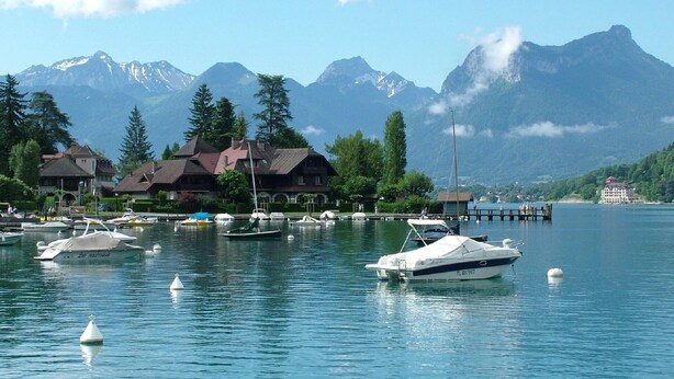 Un hôtel situé au bord d’un lac, avec plusieurs bateaux amarrés, entouré de montagnes et d’arbres.