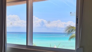 Een kamer met een raam dat uitkijkt op een turquoise oceaan en een heldere lucht.