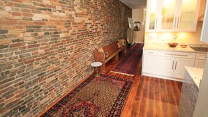 A kitchen with a brick wall, wooden floor, white cabinets, and a patterned rug. - In the Heart of Historic Downtown Paris KY (Paris)