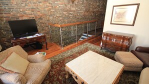 A living room with a brick wall, a flat-screen TV, a wooden coffee table, and patterned sofas. - In the Heart of Historic Downtown Paris KY (Paris)