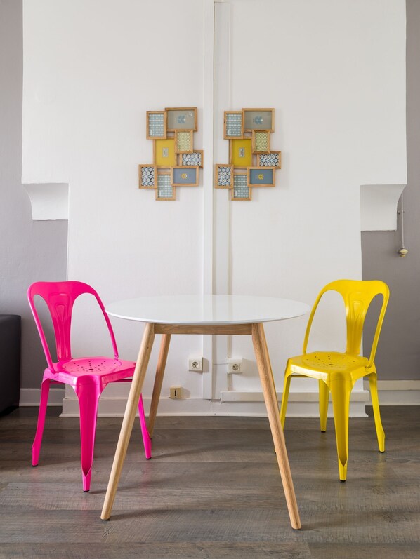 A room with a round white table, two chairs (one pink, one yellow), and a wall with framed pictures. - Nice Furnished Apartment Close to Amenities (Villeurbanne)